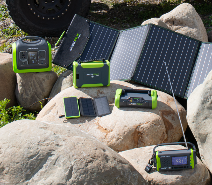 Full, six product, JackPak line up displayed in the sun on boulders with an off road vehicle tire in the distance behind them