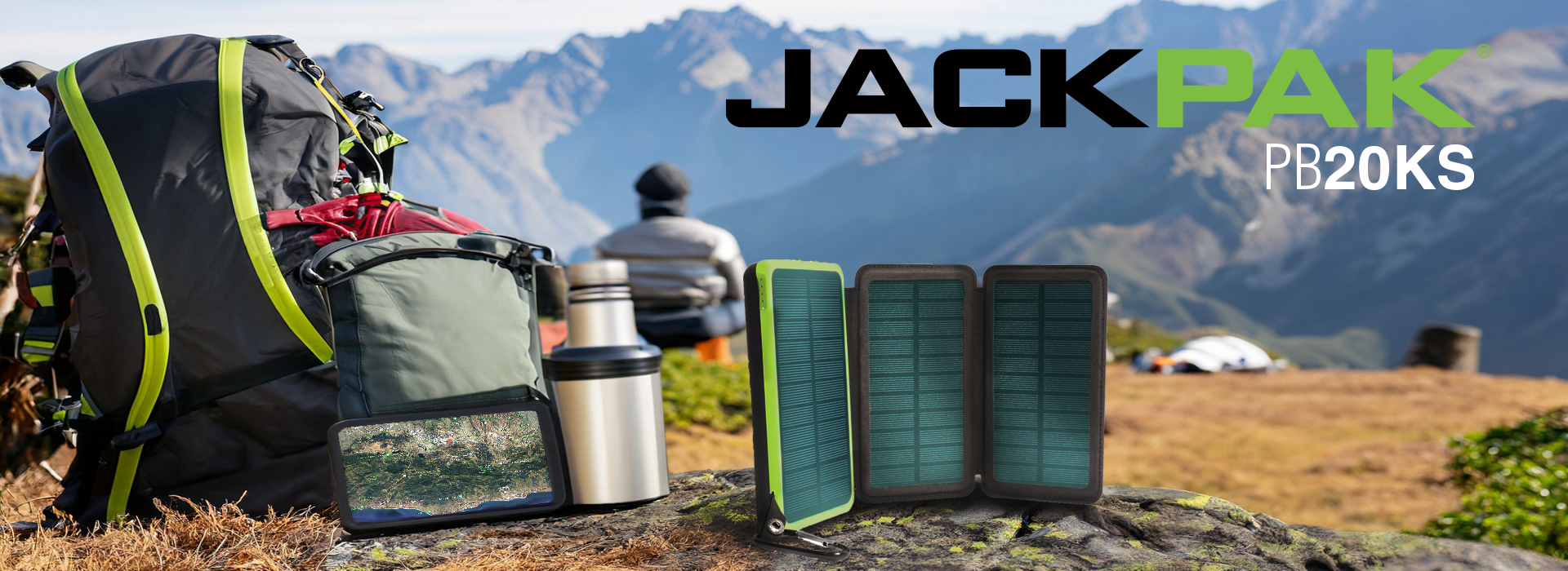 Green and black solar powered power pack on a rock next to a phone and backpack with a person in the backround enjoying a mountain view